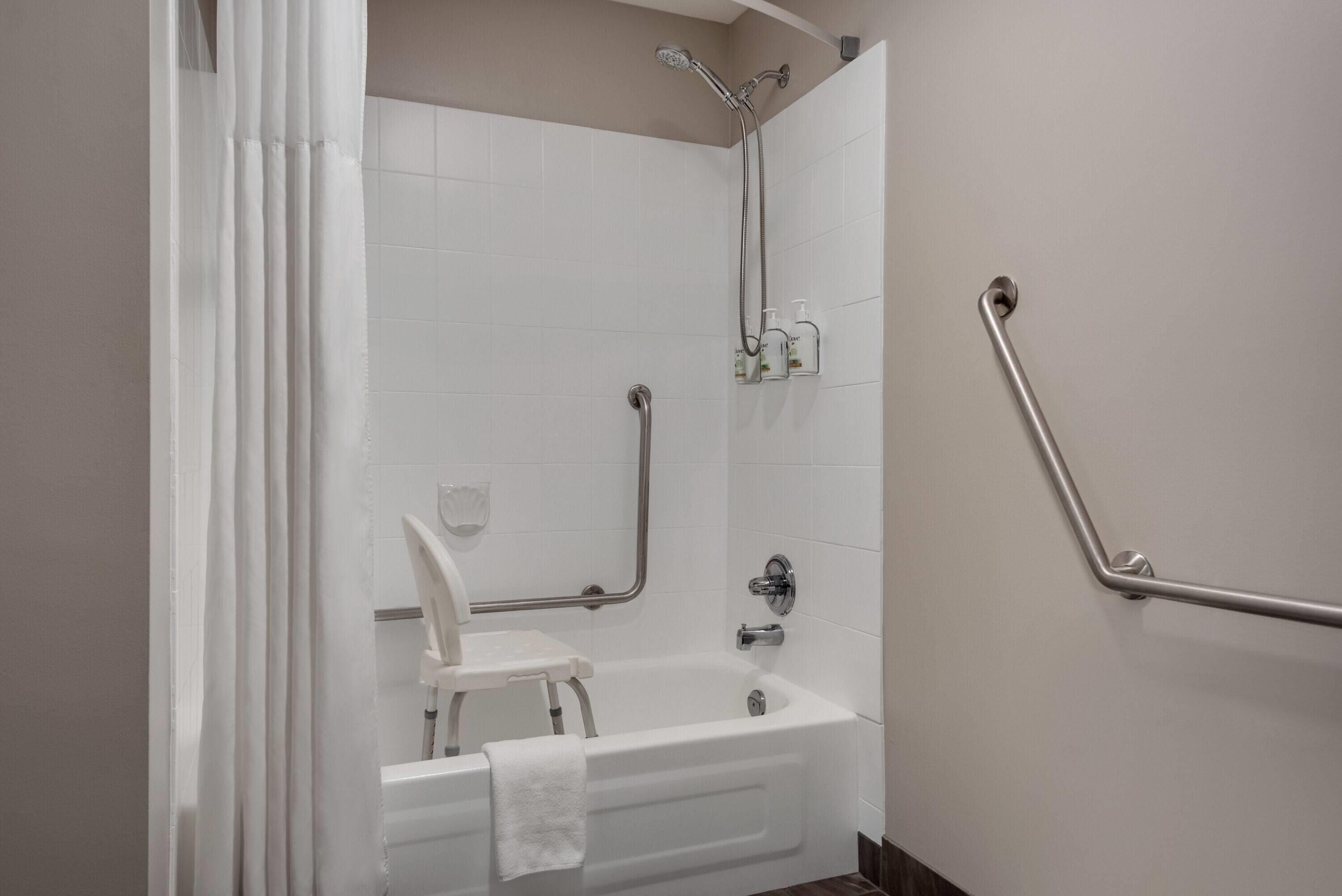 A bathroom with a white bathtub, a shower with a handheld showerhead, and a grab bar on the wall.