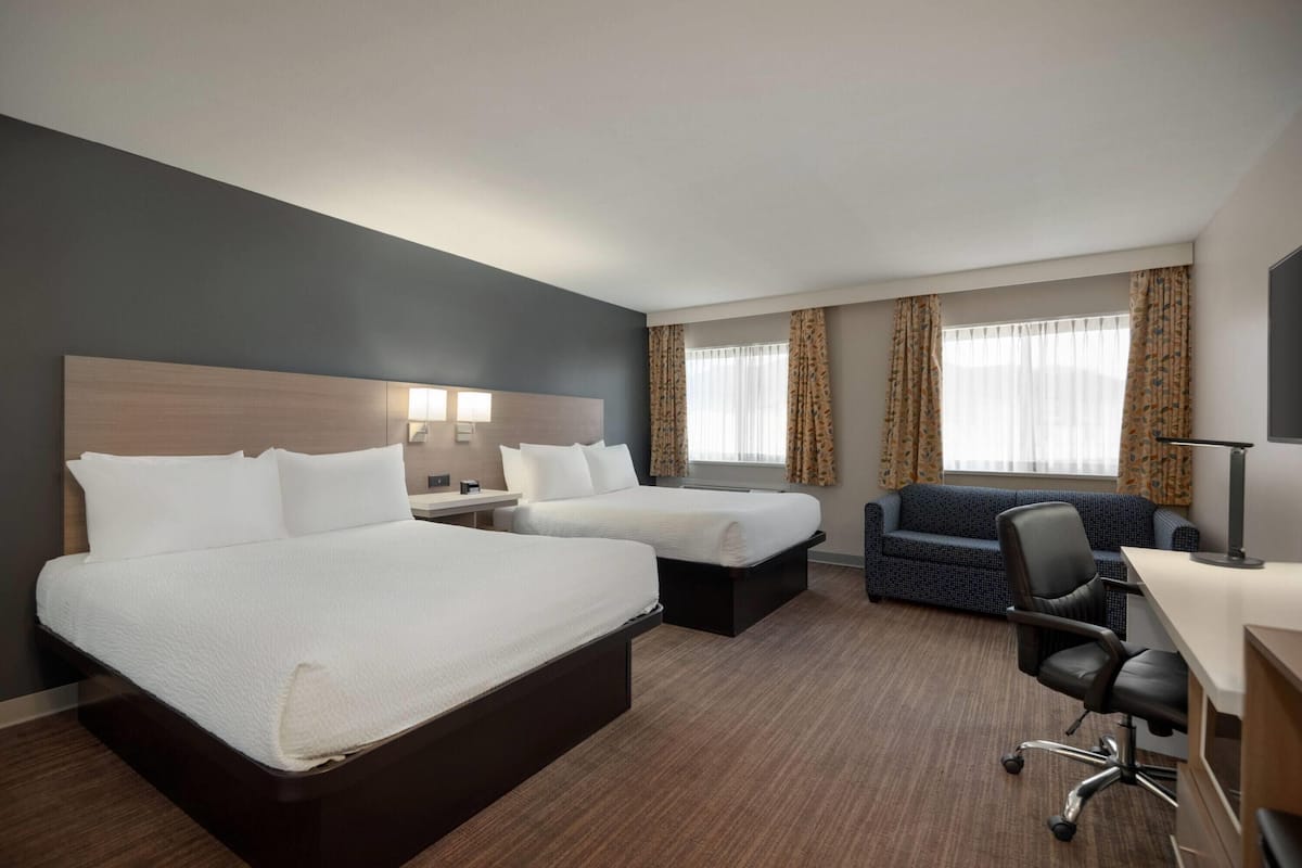 A hotel room with two beds, a sofa, a desk, and a chair.