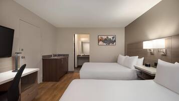 A hotel room with two beds, a desk, a chair, a TV, a sink, and a mirror.