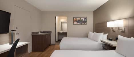 A hotel room with two beds, a desk, a chair, a TV, a sink, and a mirror.