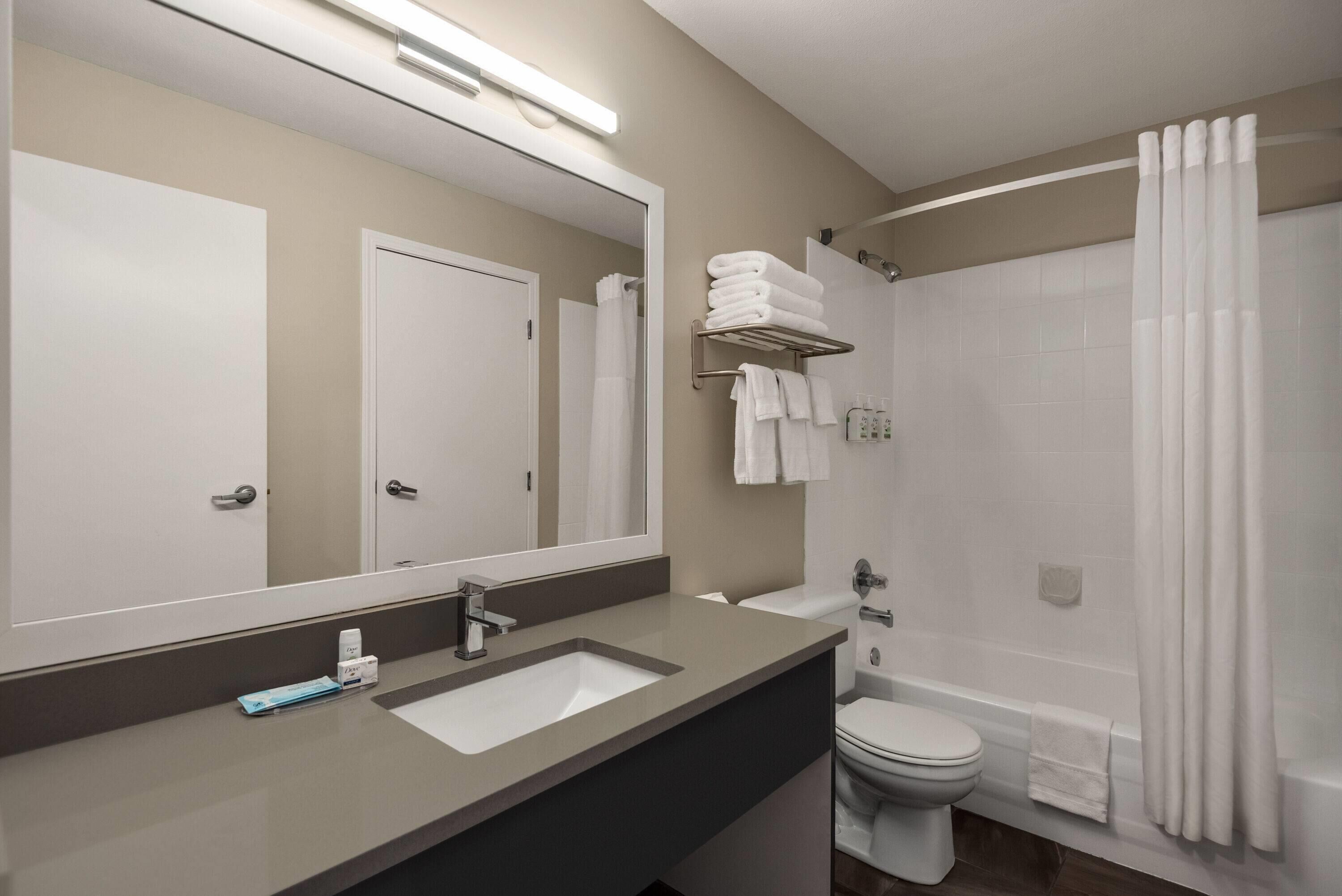 A modern bathroom with a large mirror, a sink, a toilet, and a shower area.