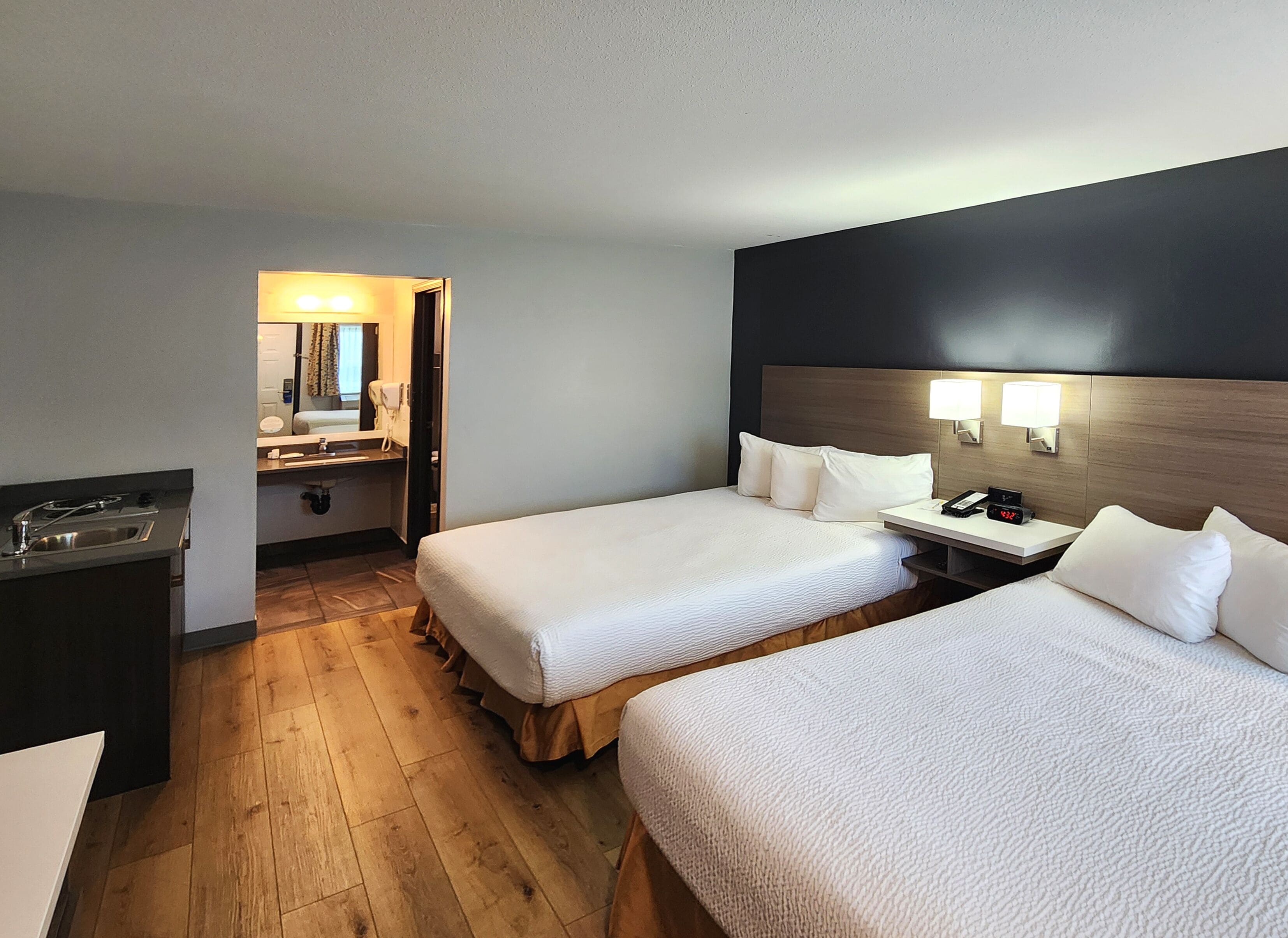 Habitación de hotel con dos camas, un escritorio pequeño, un lavamanos y un espejo.