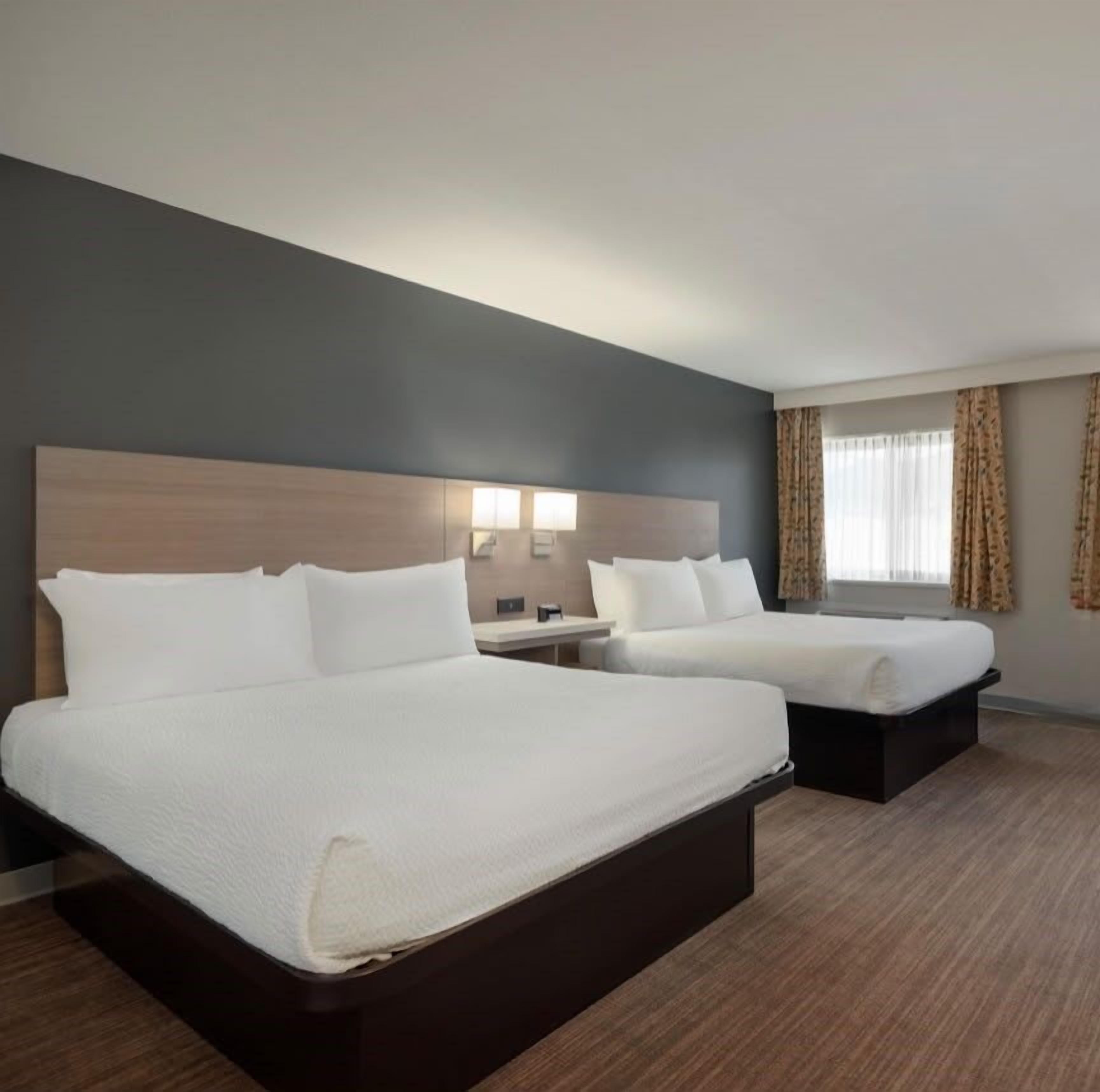 Une chambre d’hôtel avec deux lits, une table de chevet, une lampe et une fenêtre avec des rideaux.