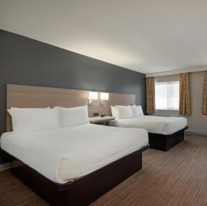 A hotel room with two beds, a nightstand, a lamp, and a window with curtains. - Days Inn by Wyndham Kelowna (Kelowna)