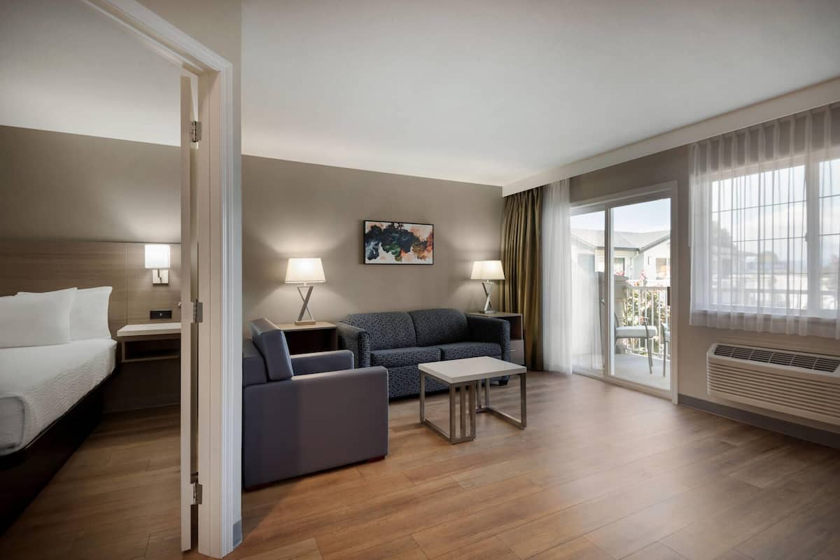 A hotel room with a bed, a sofa, a coffee table, and a painting on the wall.