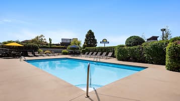 A swimming pool with lounge chairs and umbrellas, surrounded by greenery and a Days Inn sign.