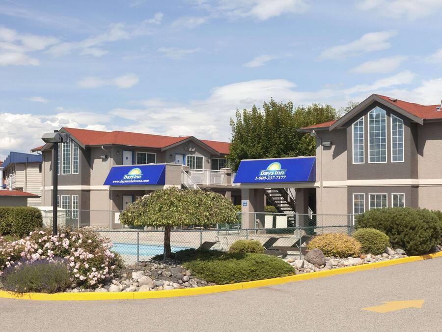 A Days Inn hotel with a red roof, multiple windows, and a landscaped area with flowers and shrubs.