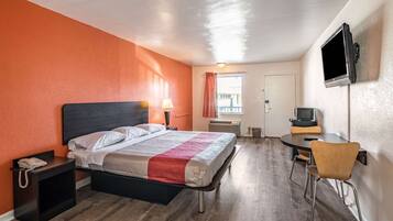 A hotel room with a bed, bedside table with a phone, a desk with a chair, a TV mounted on the wall, and a window with curtains.