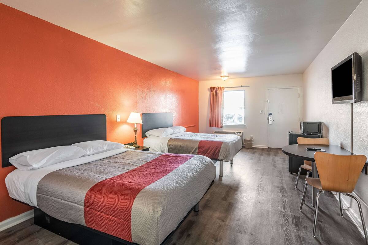 A hotel room with two beds, a desk, a chair, and a television.