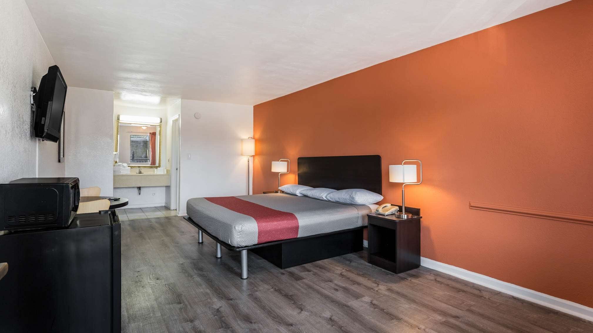 A hotel room with a bed, bedside lamps, a desk with a computer, and a mirror.