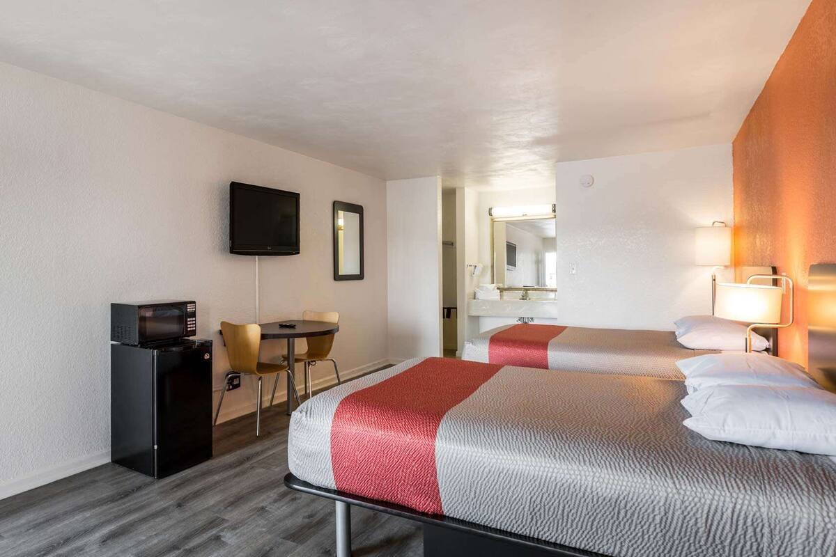 A hotel room with two beds, a desk with a computer, a TV, and a mirror.
