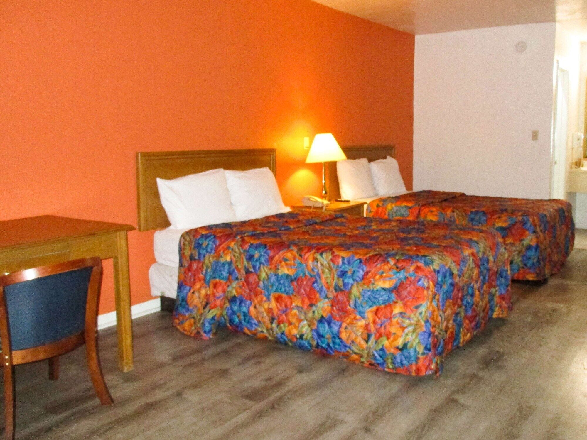 A hotel room with two beds, a wooden desk, and a chair.