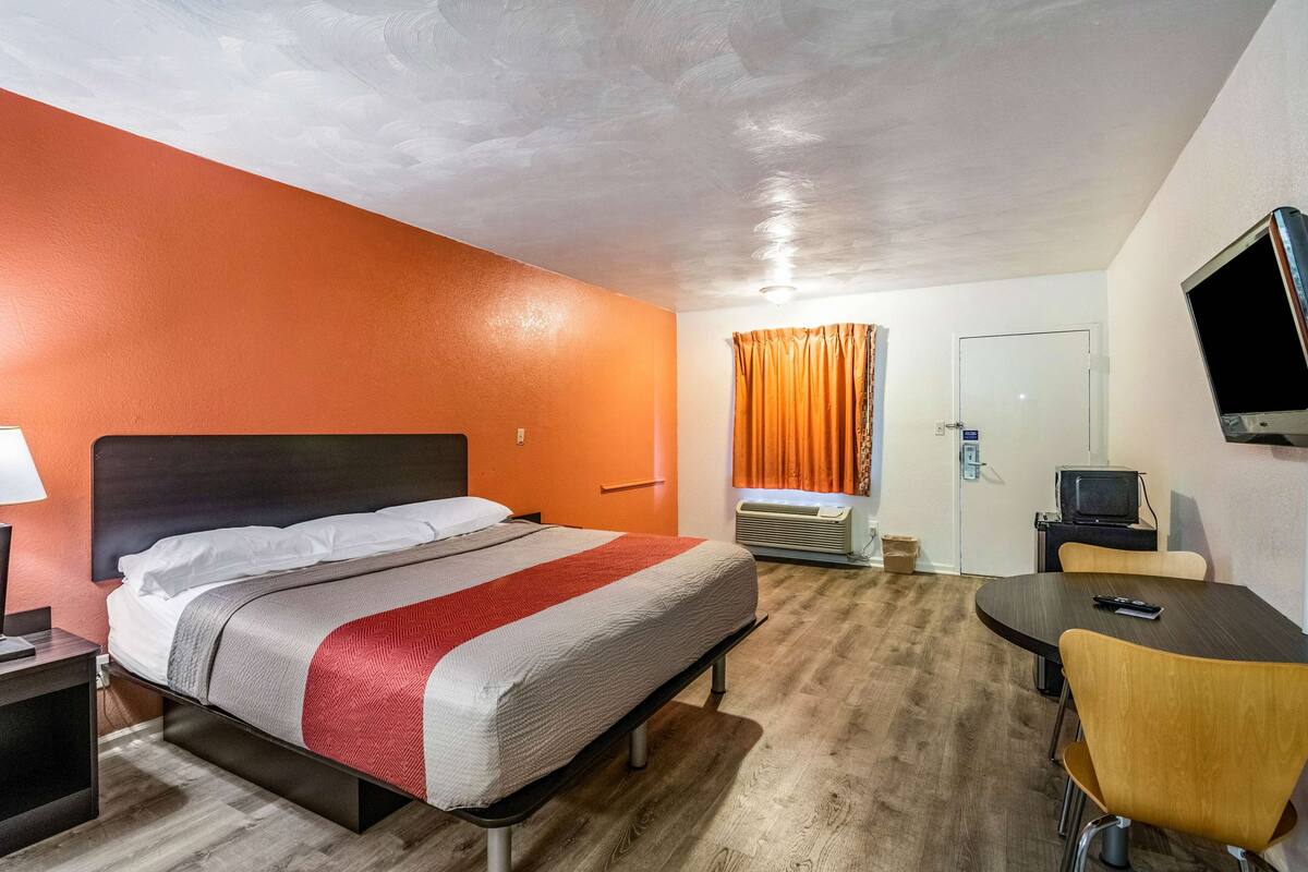 A hotel room with a bed, a desk, a chair, a TV, and a window with curtains.