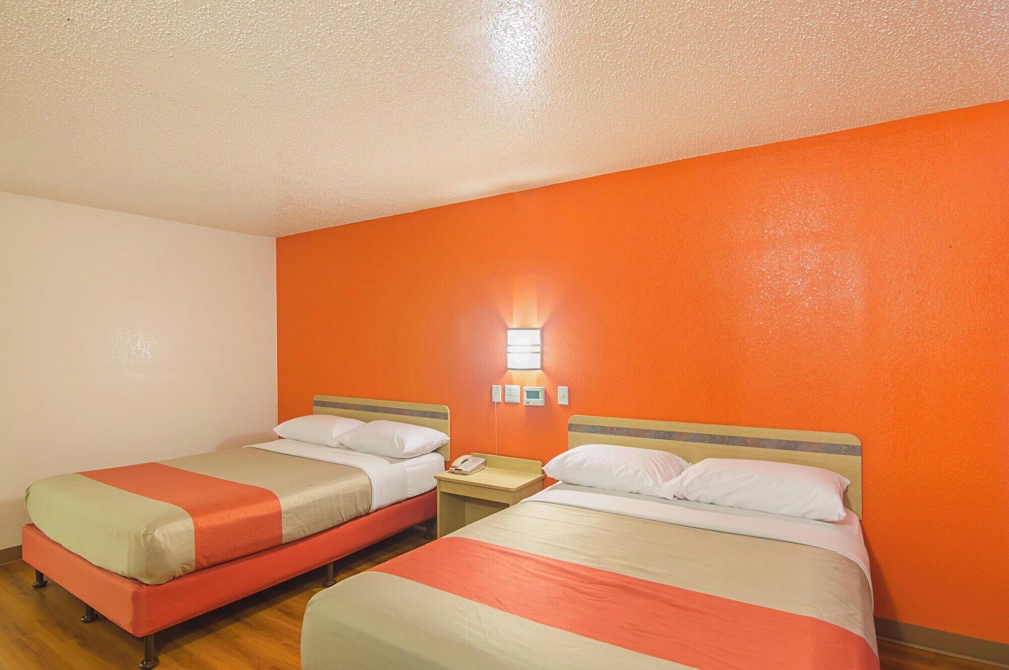Une chambre d’hôtel avec deux lits, chacun recouvert d’une couverture rouge et beige, et une petite table de chevet avec un téléphone.