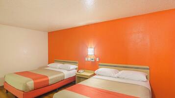Une chambre d’hôtel avec deux lits, chacun recouvert d’une couverture rouge et beige, et une petite table de chevet avec un téléphone.
