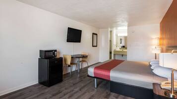 Habitación de hotel compacta con cama, escritorio con microondas, televisor y una pequeña mesa con sillas.