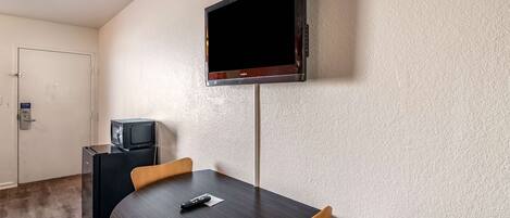 A room with a round table, two chairs, a television mounted on the wall, and a small black refrigerator.