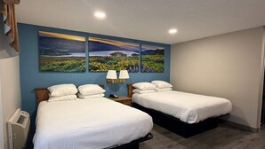 Ein Zimmer mit zwei Betten, einem Nachttisch mit Lampe, einem an der Wand montierten Heizgerät und einem großen Landschaftsbild über den Betten.