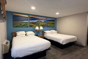 A room with two beds, a nightstand with a lamp, a wall-mounted heater, and a large landscape painting above the beds. - Days Inn by Wyndham Medford (Medford)