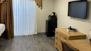 A hotel room with a wooden desk, a television mounted on the wall, and a window with curtains. - Days Inn by Wyndham Medford (Medford)