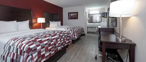 A hotel room with two beds, a desk, a chair, a lamp, a TV, and a bathroom.