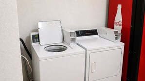 Eine Waschmaschine mit Frontlader und ein Trockner in einem Waschraum mit einem roten Coca-Cola Kühlschrank.