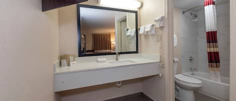 Baño con lavamanos blanco, espejo y retrete. Se aprecia una cortina de ducha y un tendedero con toallas.