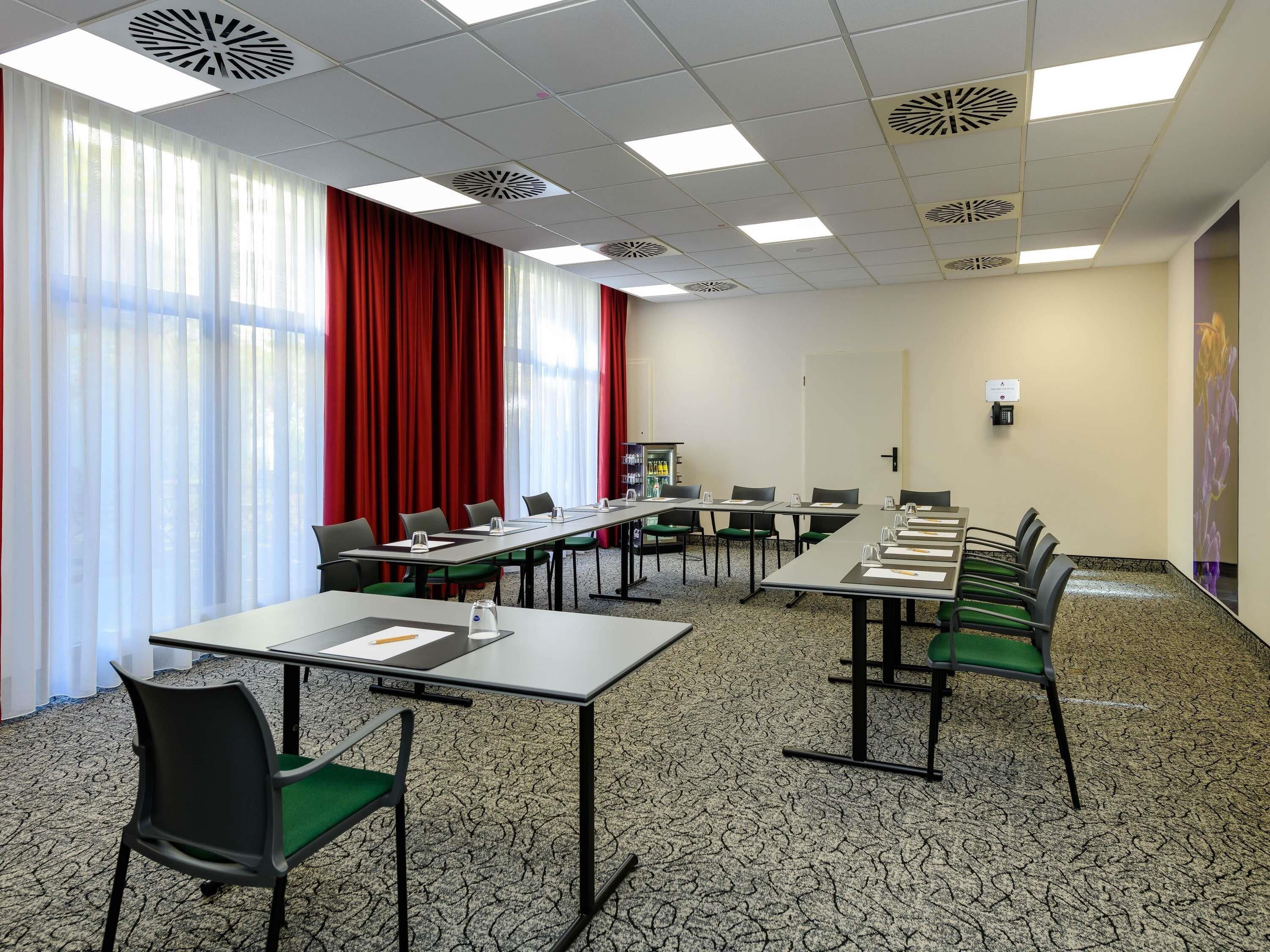 A conference room with a long table, chairs, a projector screen, and a carpeted floor.