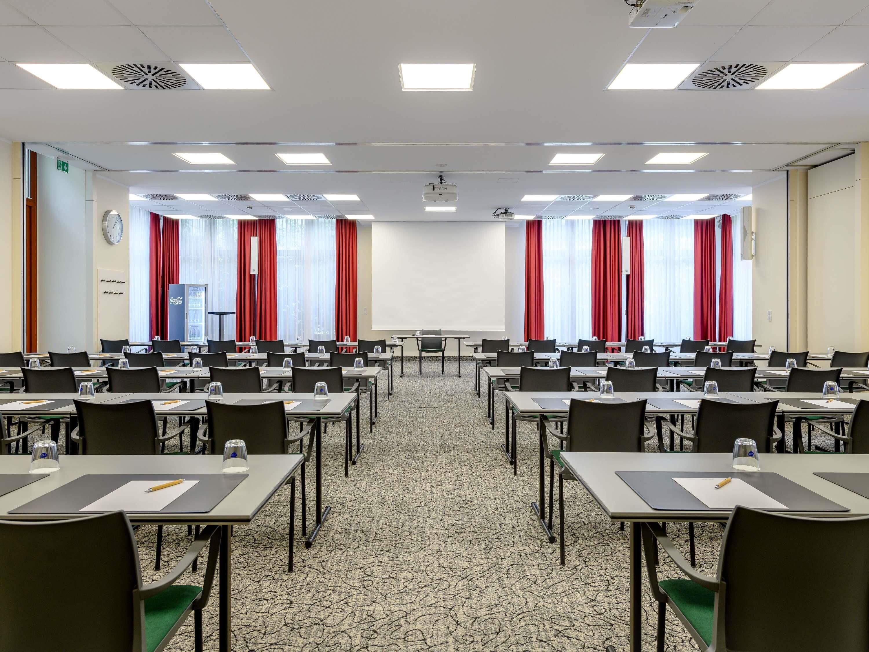 Un salón de conferencias con varias mesas, sillas, un proyector y una pantalla.