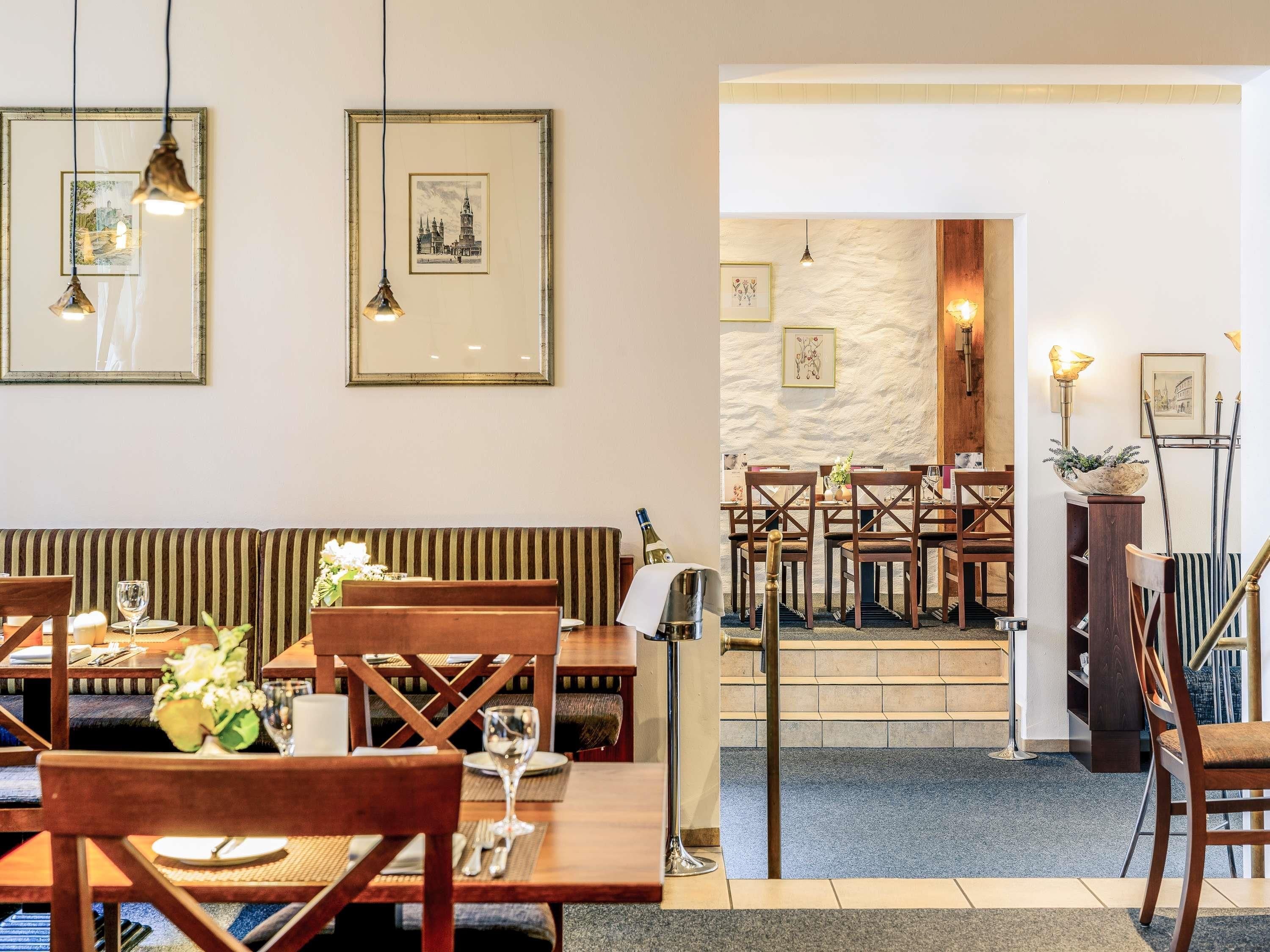 Un comedor con mesas y sillas de madera, cuadros en la pared y una pared de piedra al fondo.