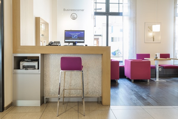 Un espace d’accueil comprenant un écran d’ordinateur, une imprimante et un coin salon avec des chaises.