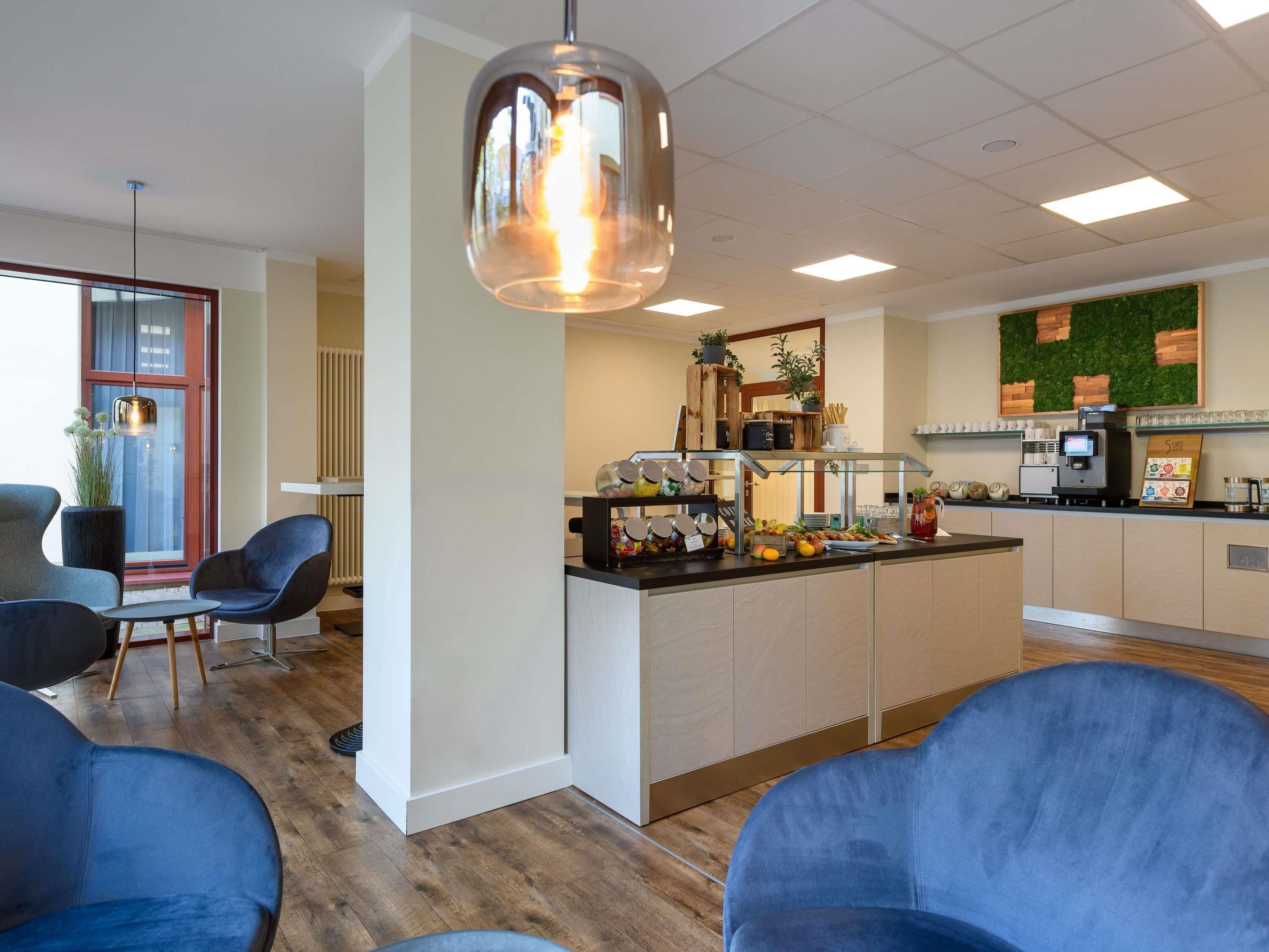 A modern cafe with a wooden counter, blue chairs, and a green wall decoration.