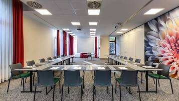 Une salle de conférence avec une longue table, des chaises, un projecteur et une grande fresque florale sur le mur.