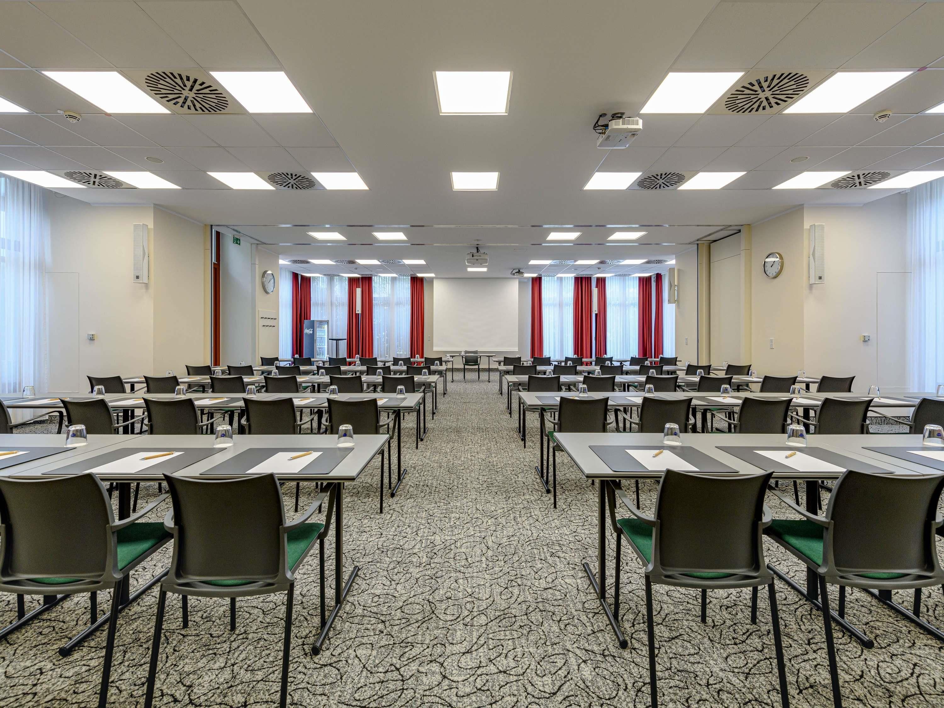 Una sala conferenze con diversi tavoli, sedie, un proiettore e una sveglia appesa al muro.