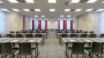 Una sala conferenze con diversi tavoli, sedie, un proiettore e una sveglia appesa al muro.