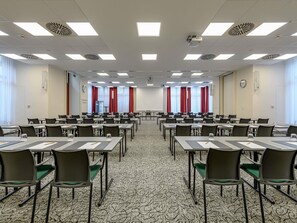 Uma sala de conferências com várias mesas, cadeiras, um projetor e um relógio na parede.