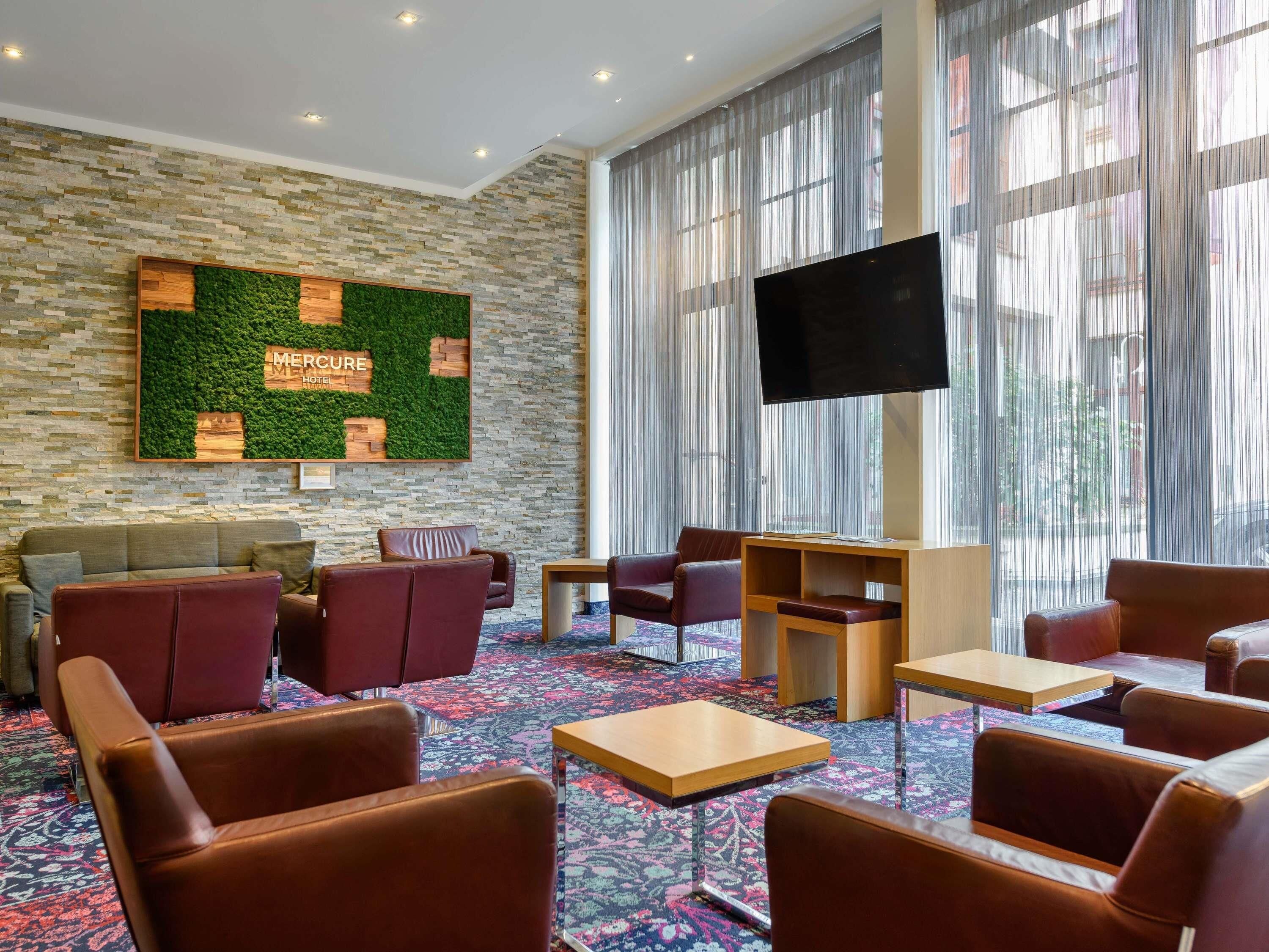Eine Hotelhalle mit Steinwand, einer grünen Wand mit Text, Ledersesseln, einem Fernseher und großen Fenstern.