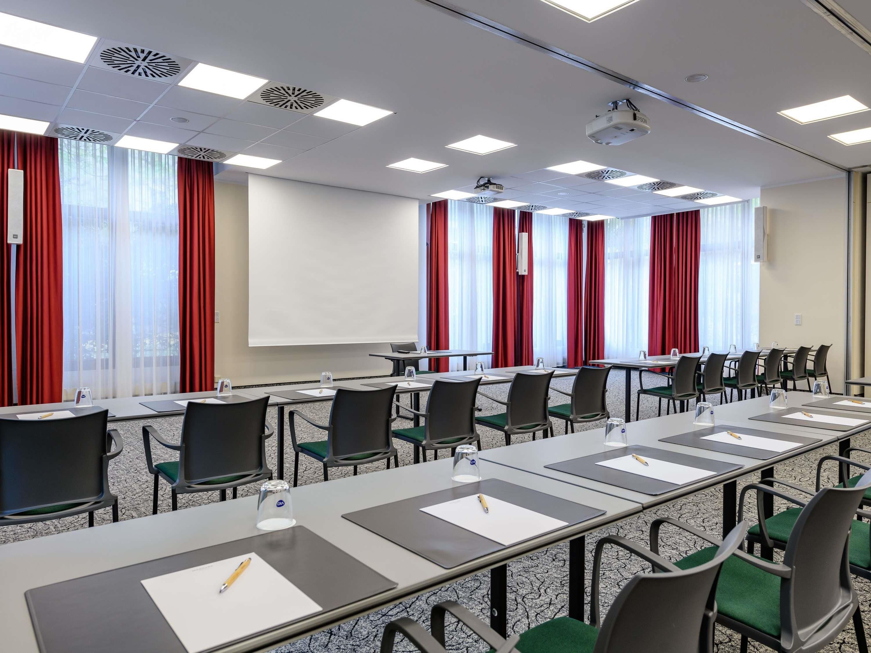 A conference room with a long table, chairs, a projector, and a screen.