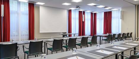 A conference room with a long table, chairs, a projector, and a screen.