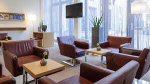 A modern hotel lobby with leather seating, a flat-screen TV, and large windows. - Mercure Hotel Erfurt Altstadt (Erfurt)