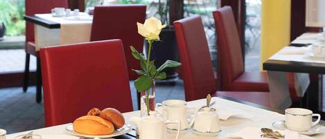 Un desayuno montado con una mesa para dos, que incluye croissants, un vaso de zumo de naranja y una rosa blanca en un jarrón.