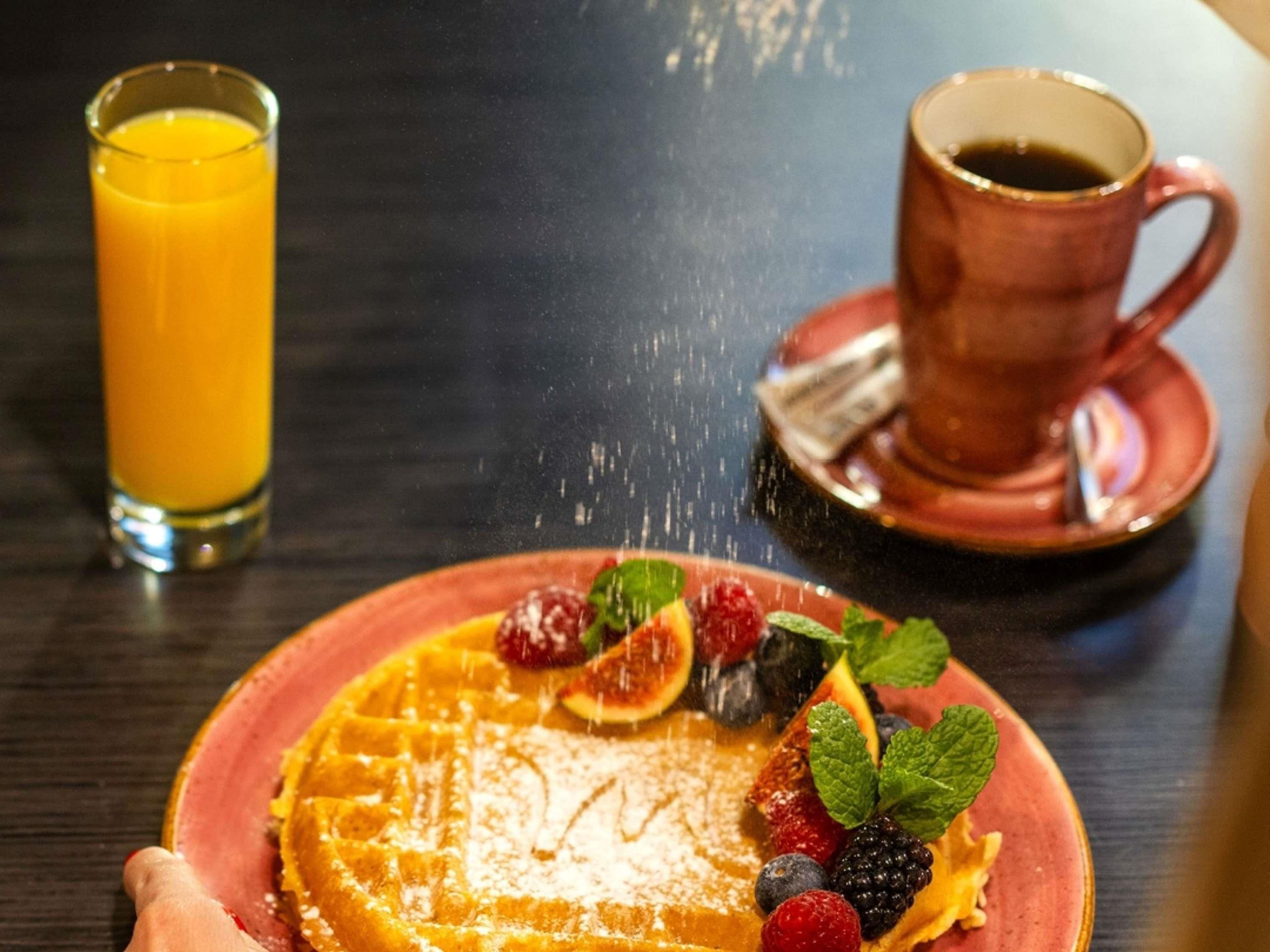 Un plato de desayuno con waffles, bayas y un vaso de jugo de naranja.