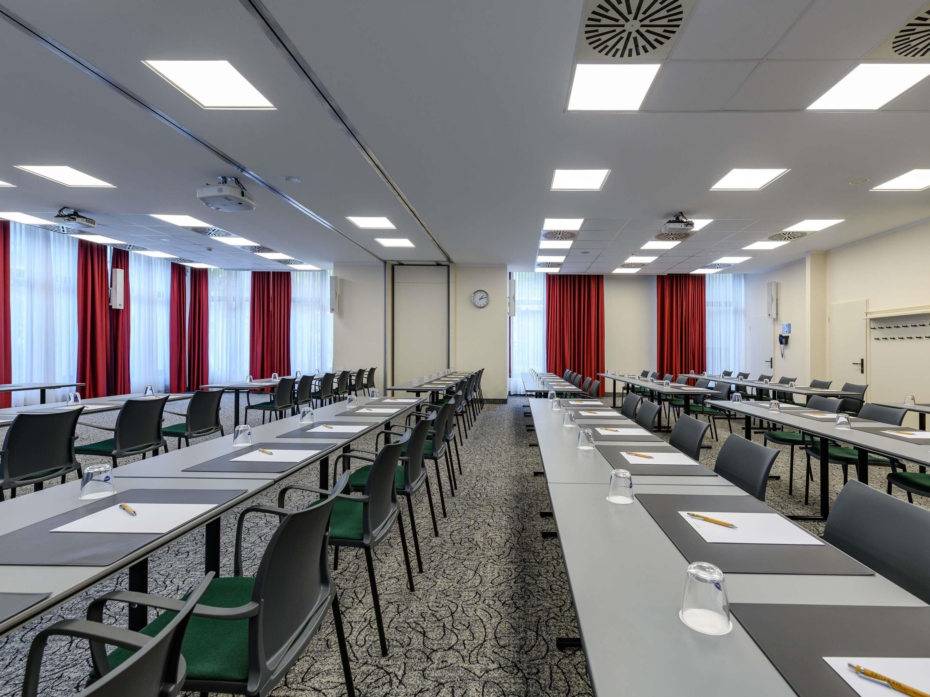 Une salle de conférence équipée de longues tables, de chaises et d’un écran de projection.