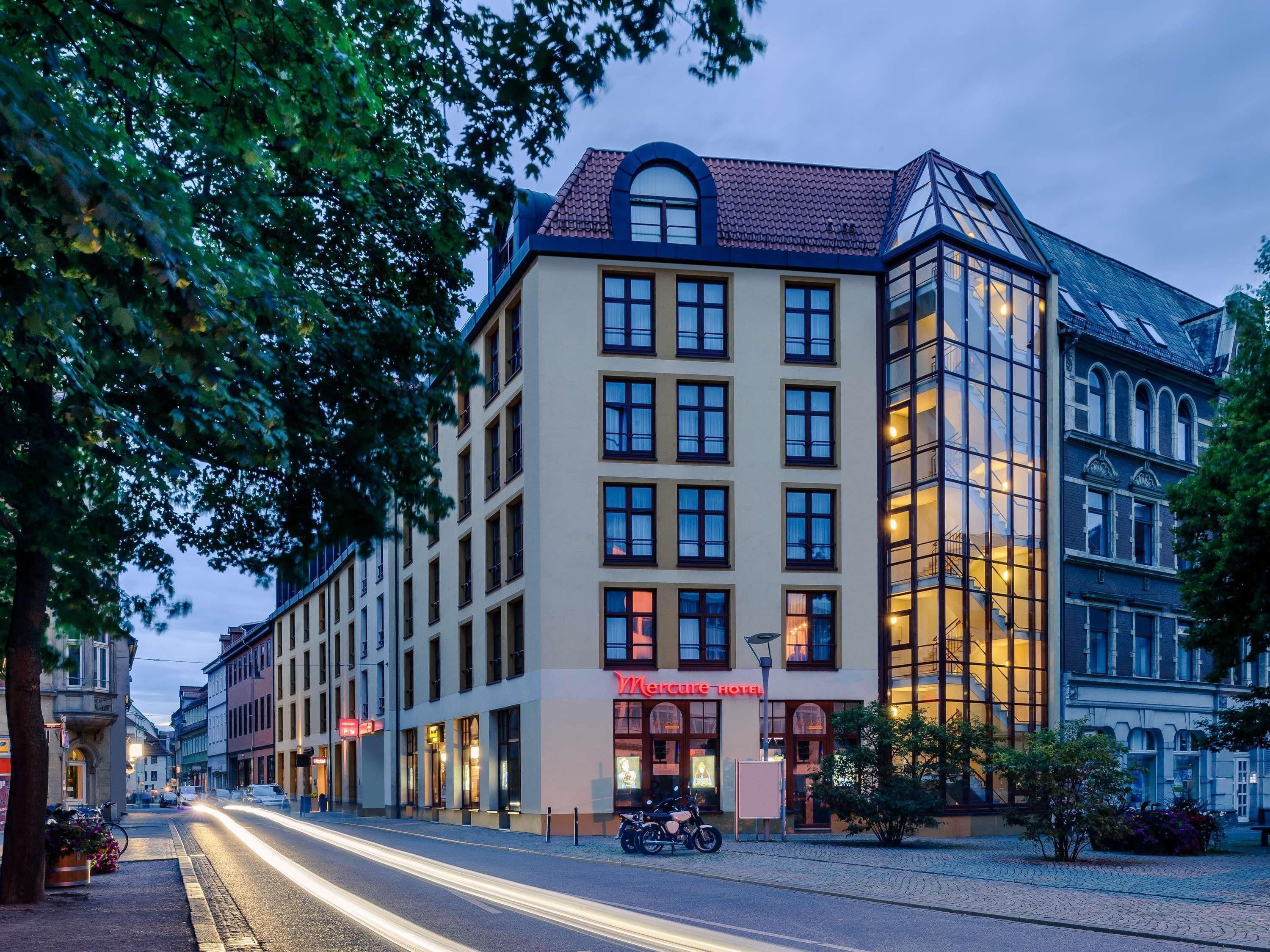 A hotel with a classic architectural style, featuring a prominent corner entrance with a glass facade and a tiled roof.