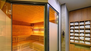 Un sauna avec des bancs en bois et une porte en verre, un porte-serviettes avec des serviettes soigneusement pliées, et une horloge au mur.