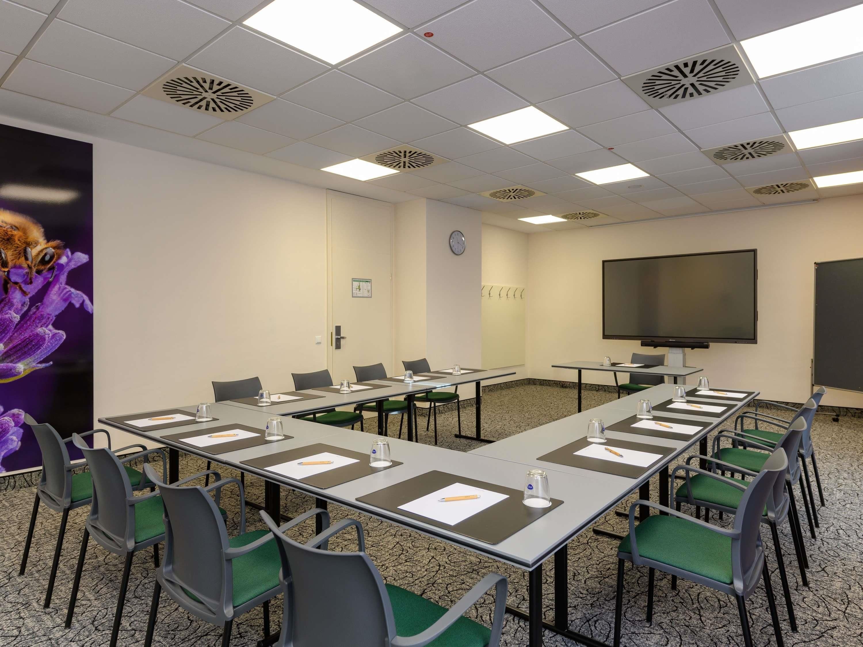 A conference room with a long table, chairs, a projector screen, and a clock on the wall.