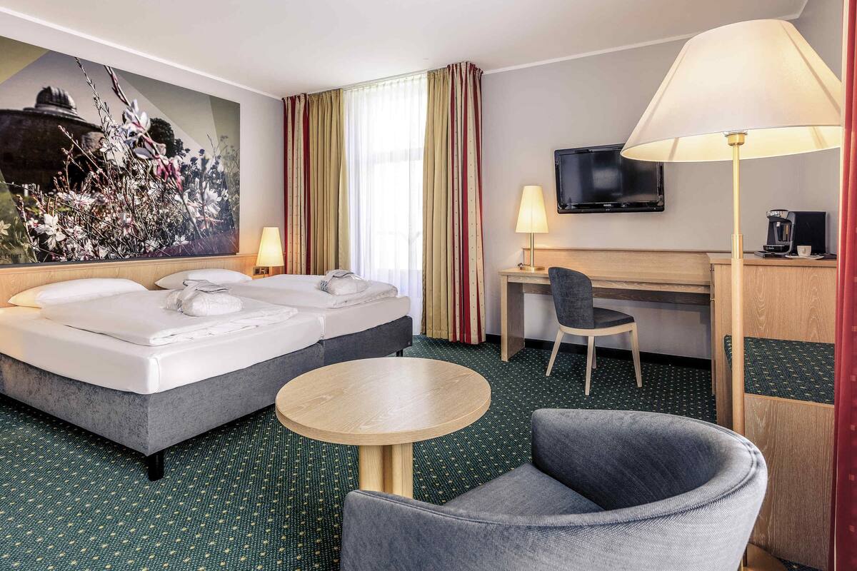 Una habitación de hotel con cama, escritorio, silla, televisor y obras de arte.