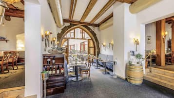 A restaurant with a rustic interior, featuring exposed wooden beams, a central seating area with tables and chairs, and a wine display.