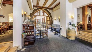 Un restaurant au décor rustique, avec des poutres apparentes, un espace central aménagé avec des tables et des chaises, et un présentoir à vins.