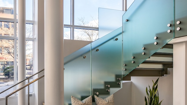 Un escalier moderne avec des rampes en verre, un banc agrémenté de coussins à motifs et des luminaires suspendus.